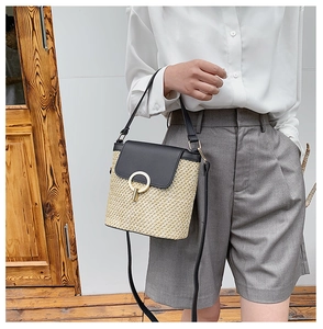 Detail of straw bucket bag featuring a black leather flap and golden round buckle
