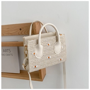 Détail d'un sac cabas en paille tissée avec broderie marguerite et anses en similicuir
