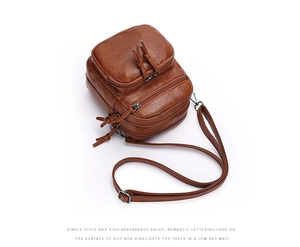 Detail view of caramel brown multi-pocket crossbody bag with tassel zippers and soft texture