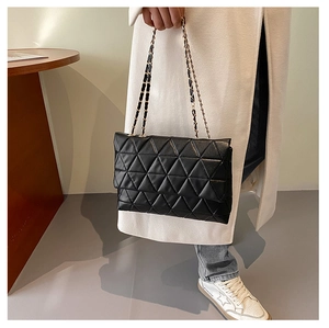 Détail d'un sac bandoulière noir à matelassage triangulaire tenu par un mannequin en salle