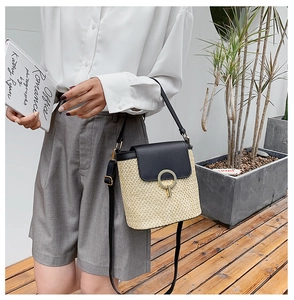 Detailed outdoor shot of a beige straw bucket bag with black leather flap and gold clasp