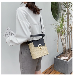 Detail of straw bucket bag featuring black leather flap and golden ring buckle closure