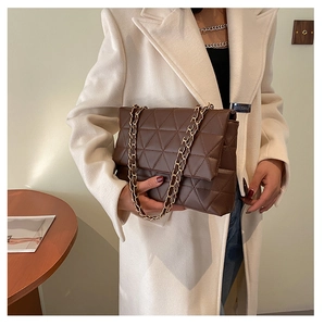 Détail du sac matelassé marron foncé avec chaîne dorée porté sur un manteau de couleur crème