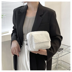 Détail du petit sac à bandoulière en fausse fourrure blanche avec rabat sur costume noir