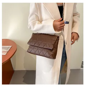 Détail d'un sac bandoulière marron foncé matelassé avec chaîne dorée et coutures triangles