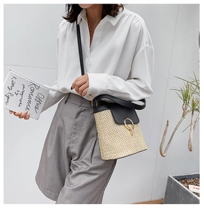 Detail of straw and black leather bucket bag with golden metal ring buckle on model