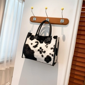 Detail van een tote bag met koeienprint hangend aan een houten haak in woonkamer