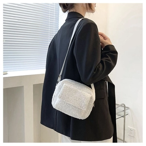 Vue détaillée d'un sac bandoulière blanc en laine d'agneau porté sur un blazer noir