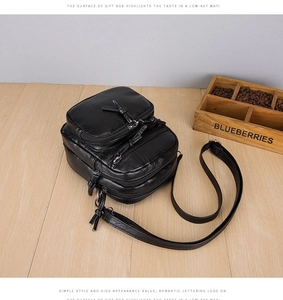 Detailed view of black multi-zipper crossbody bag with soft PU leather texture on wood surface