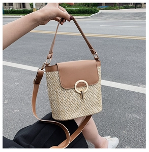 Detailed shot of straw bucket bag with brown leather trim and golden metal ring closure