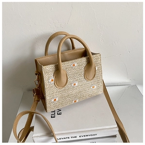 Détail du sac en paille montrant la broderie de marguerite blanche et les anses en cuir PU