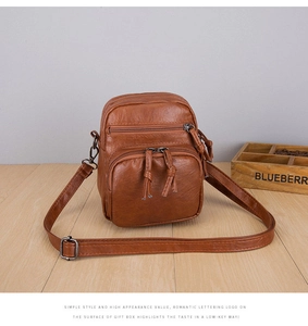 Detailed view of brown PU leather bag with multi-zipper layers and lychee grain texture