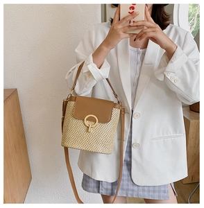 Detail of hand-woven straw bucket bag featuring a brown leather flap and golden buckle