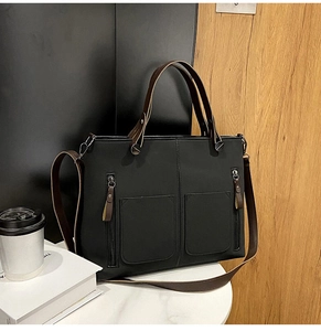 Detail of black matte handbag featuring brown leather handles and dual large front pockets