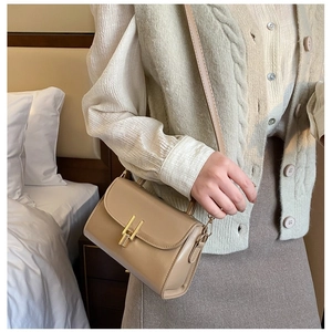 Chic beige crossbody bag with gold metal clasp on a female model in warm bedroom setting