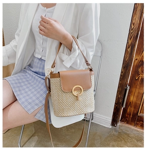 Detail view of straw bucket bag with brown leather flap and gold clasp on a model