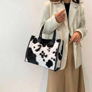 Detail van de tote bag van imitatiebont met koeprint en zwarte handvatten op het model