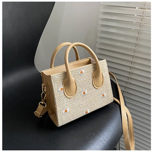 Détail d'un sac cabas en paille brodé de marguerites posé sur une chaise moderne