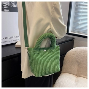 Grass green corduroy bucket bag shown on shoulder with minimalist cream suit jacket