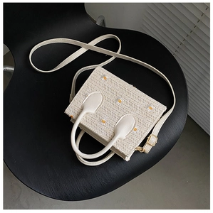 Détail d'un sac en paille avec broderie marguerite, anses en cuir et bandoulière