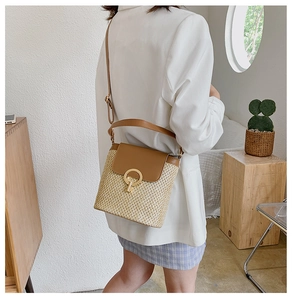 Detail of hand-woven straw bucket bag with brown leather flap and round gold ring buckle