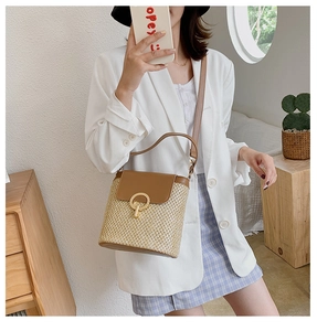 Detail of hand-woven straw bucket bag with brown leather flap and golden ring buckle