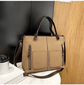 Detail of khaki tote bag featuring dual front pockets and brown leather top handles
