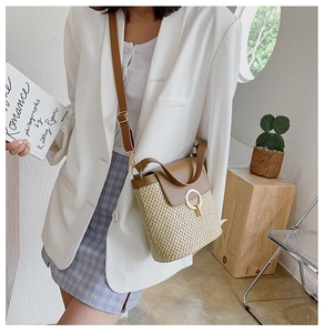 Detail of khaki straw bucket bag with brown leather flap and golden hardware on a model