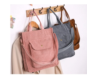 Three corduroy tote bags in pink, grey, and brown hanging on a wall for display
