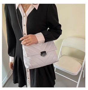 Detail showing V-quilted texture and metal buckle on a light-colored crossbody bag