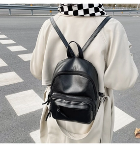 Outdoor street view of a black minimalist PU leather mini backpack with adjustable straps