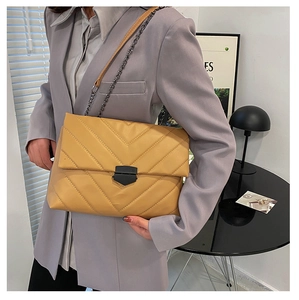 Detail of yellow quilted crossbody bag with black metal lock and chain strap