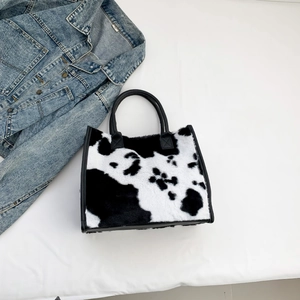 Detail van de pluche tote bag met koeprint en zwarte handvatten op een lichte achtergrond