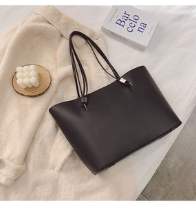 Gros plan d'un sac cabas en cuir noir sur manteau beige avec bougie et livre décoratif