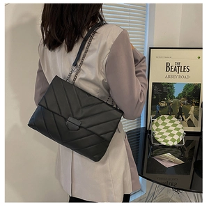 Detail of black V-quilted shoulder bag with metal chain strap worn by a model