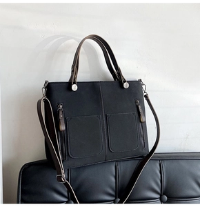 Detail of black tote bag with brown leather handles and decorative side zippers