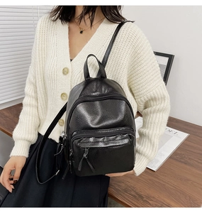 Detail of a black pebbled leather mini backpack showing triple zipper pockets and texture