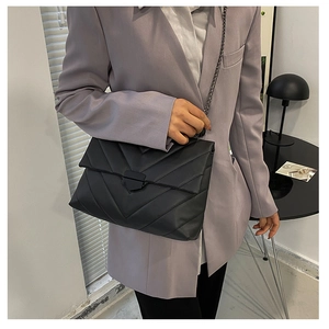 Detail of black quilted crossbody bag with V-shaped texture and metal chain strap