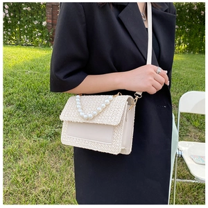 Detail of cream woven shoulder bag with pearl handle and gold hardware on green grass