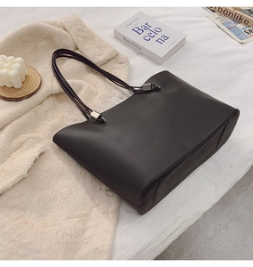 Gros plan sur un sac cabas noir minimaliste avec des anses fines et des boucles métalliques