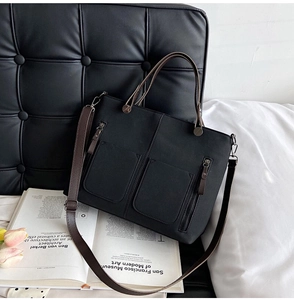 Detail of black canvas tote bag with brown handles and front pockets on a sofa