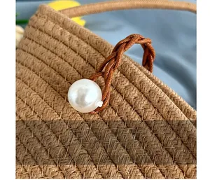 Détail macro du sac seau en paille tissée avec boucle en perle blanche décorative