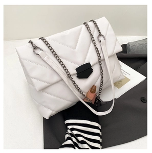 Detail of white quilted crossbody bag with metal chain strap on textured fabric