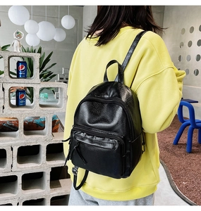 Detailed view of black pebbled leather mini backpack on model wearing yellow hoodie