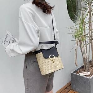 Straw bucket bag with black leather flap and gold buckle shown in a lifestyle scene