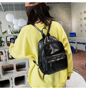 Close-up of black leather mini backpack with tassel zipper detail on yellow hoodie
