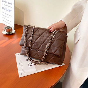 Sac à bandoulière matelassé marron foncé avec chaîne dorée sur une table en bois