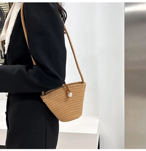 Détail du sac seau en paille tissé à la main avec un grand ornement en perle et cuir