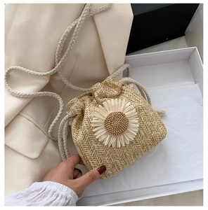 Detail of woven straw bucket bag featuring a large white daisy and cotton drawstring
