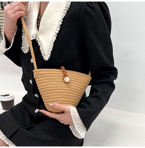 Détail d'un sac seau en paille tressée avec fermoir en perle et poignée élégante